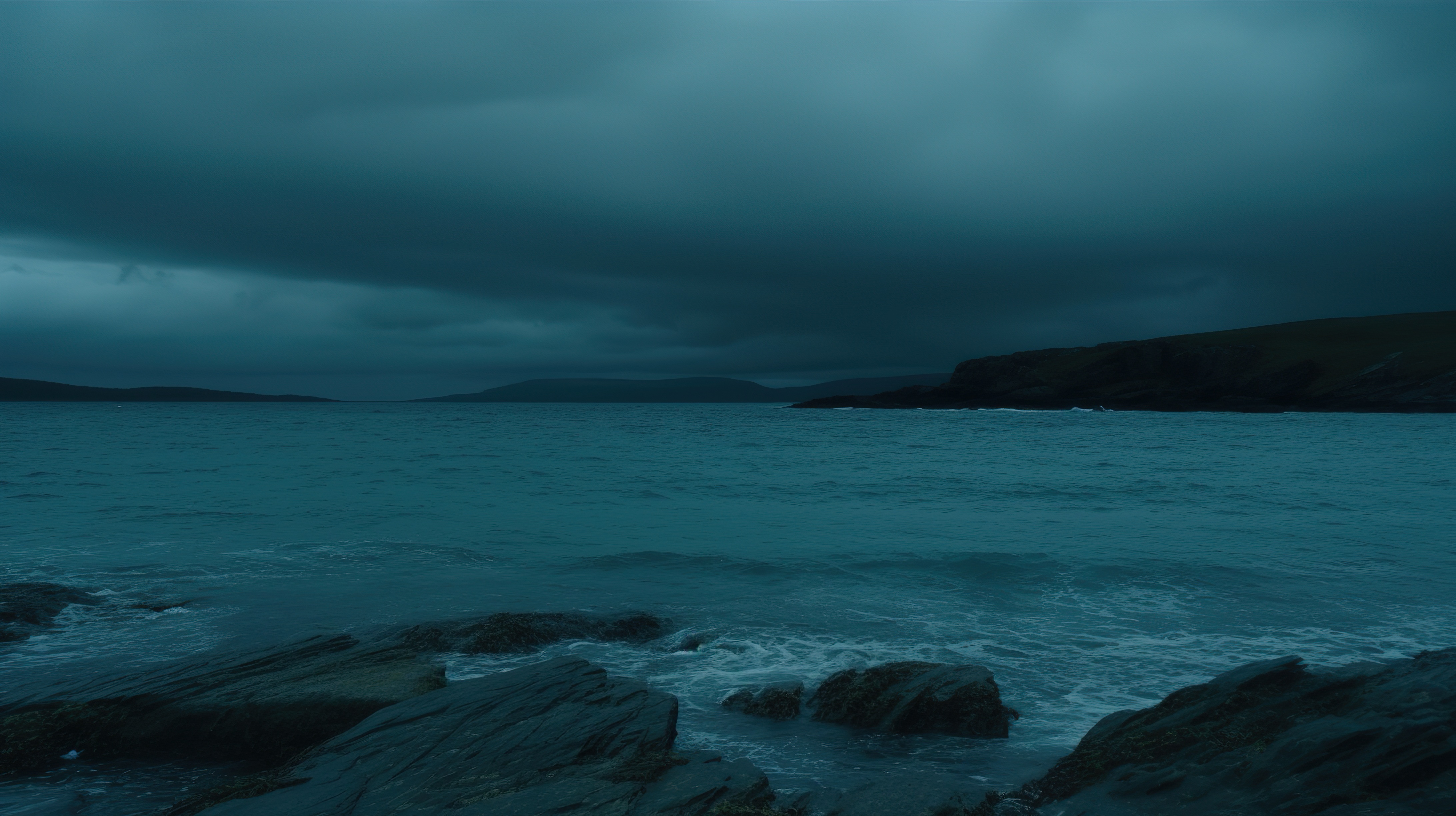 Sky with dark clouds and a beach with calm water and rocks on the shore