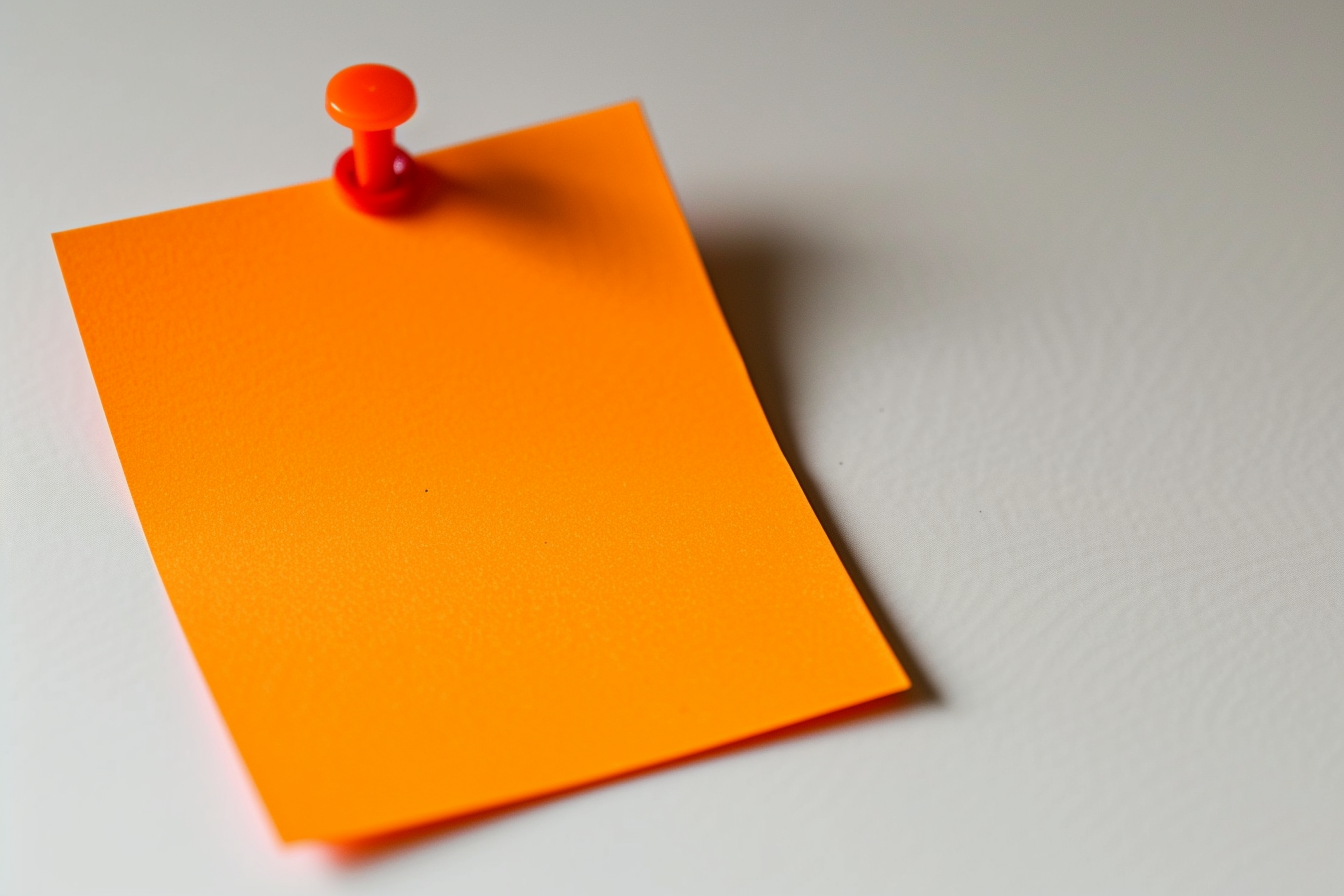 Orange colored sticky note pinned on a white background